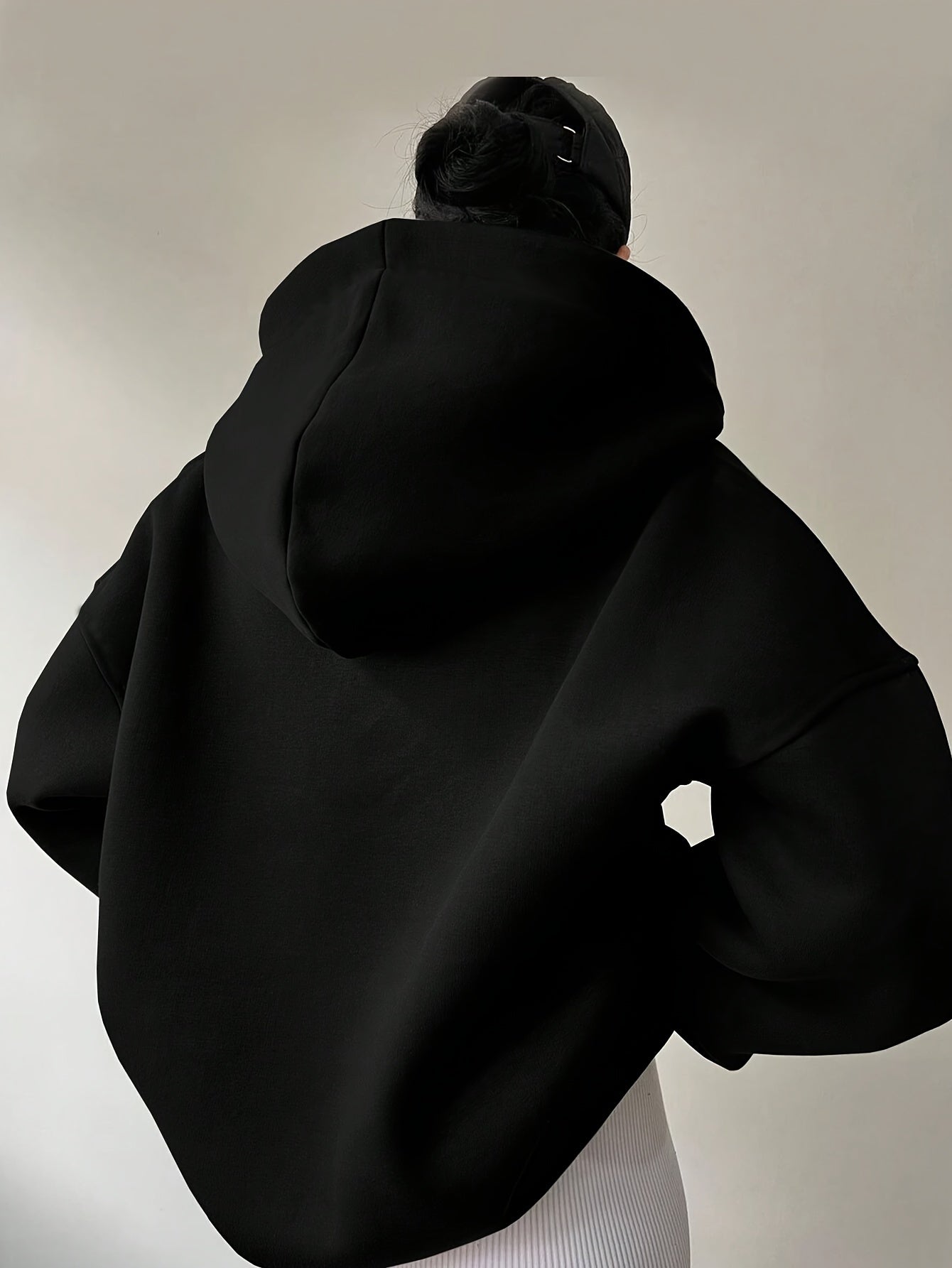 The back view of a woman wearing a black winter hoodie for women sold by 100 Spartans