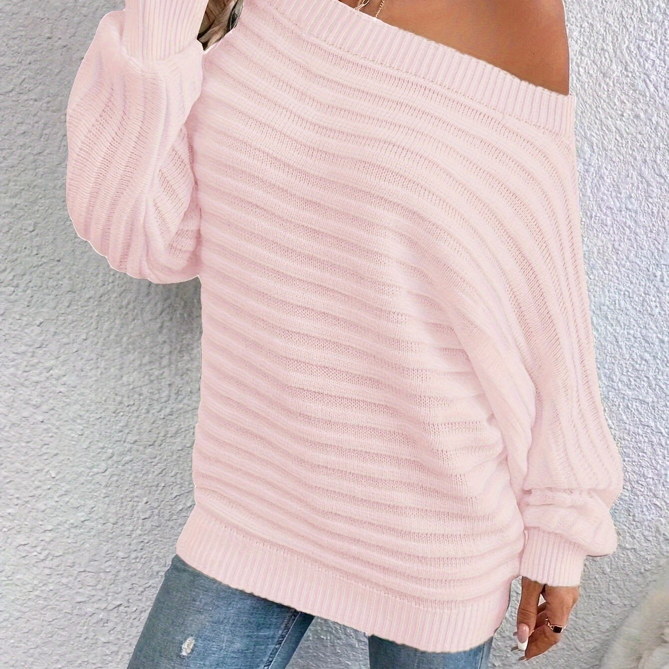 Pink off shoulder sweater worn by a person against a light gray wall.
