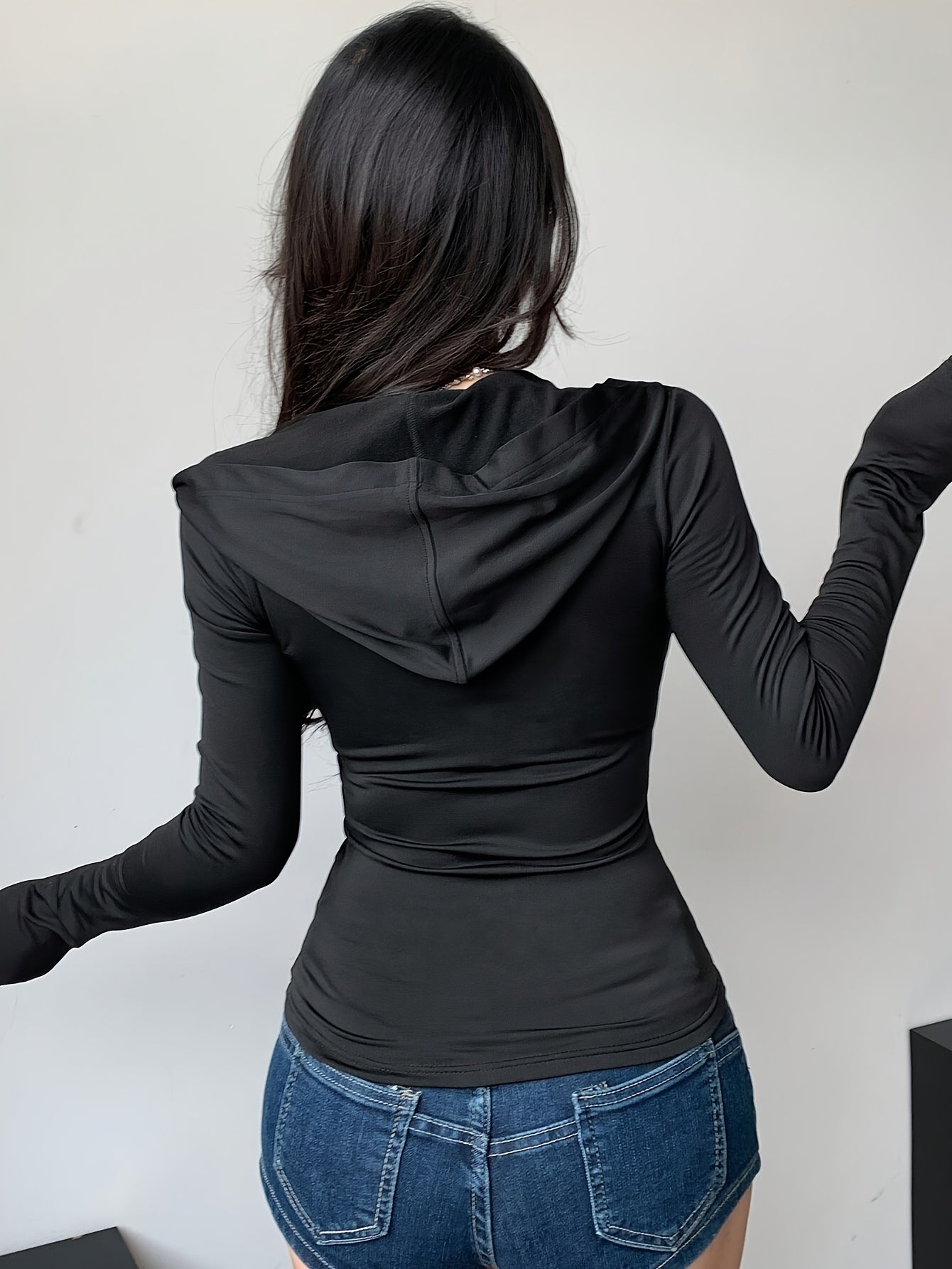 Person wearing a black long-sleeve top with a hood and blue jeans against a white background