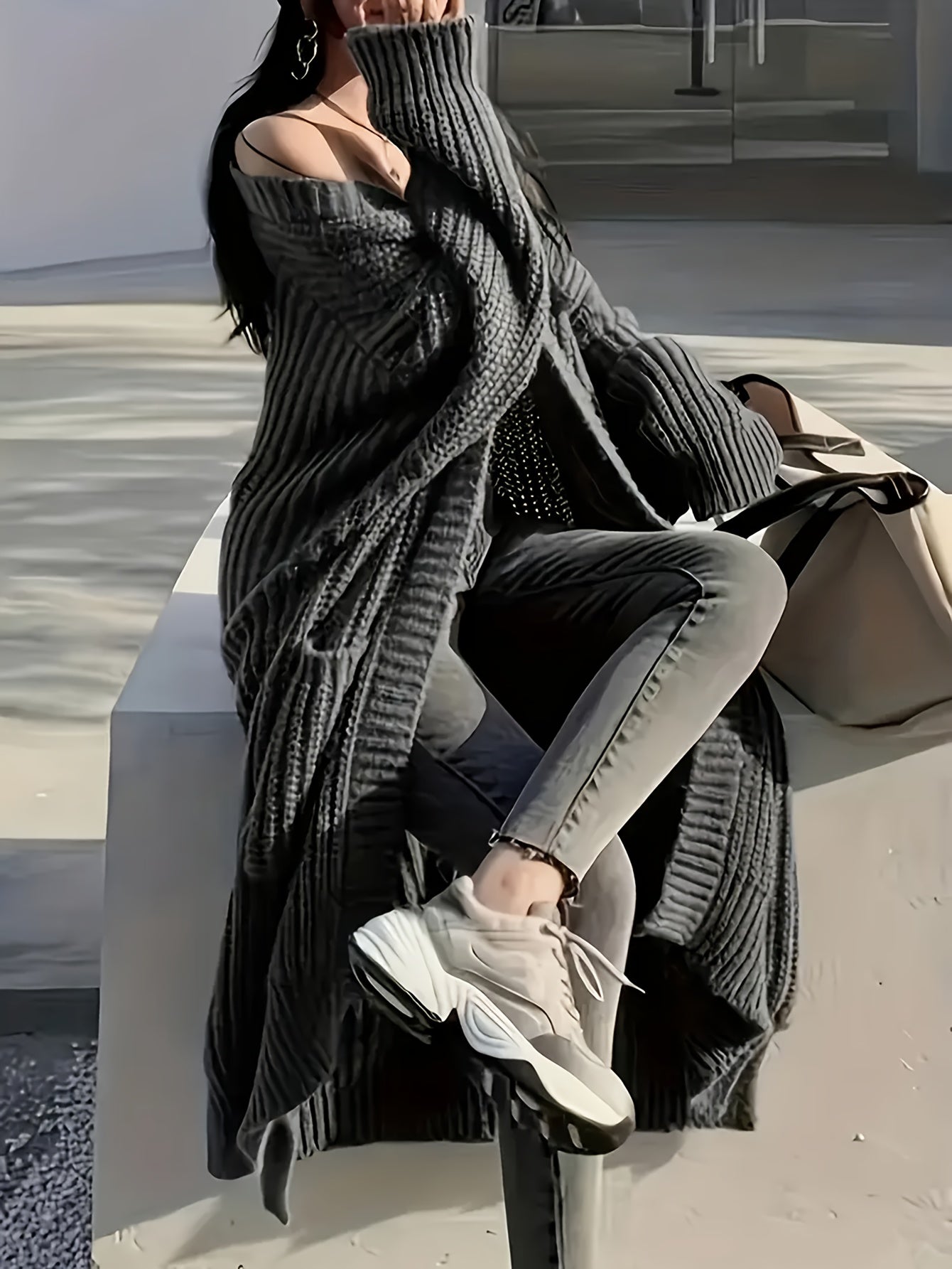 Person wearing a gray oversized sweater and light-colored pants sitting on a bench.