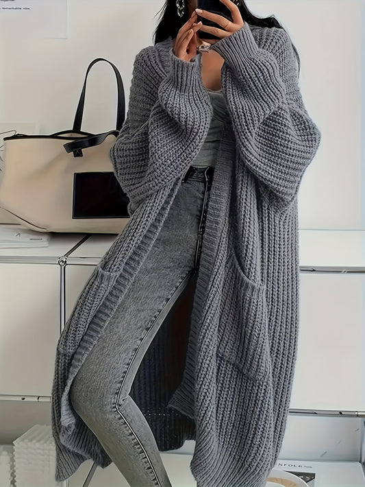 Person wearing a long gray knitted cardigan over jeans, standing against a neutral background.