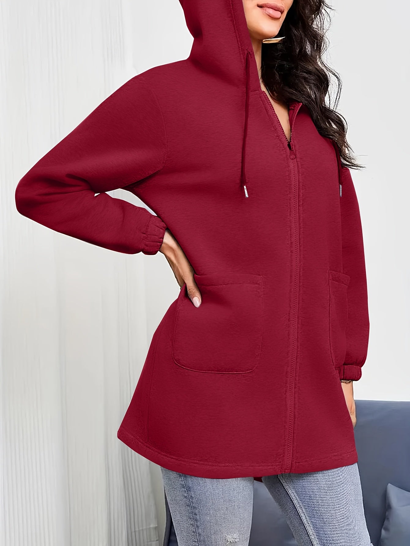 Woman wearing a red women's oversized zip up hoodies, white crop top, and blue jeans on a plain background