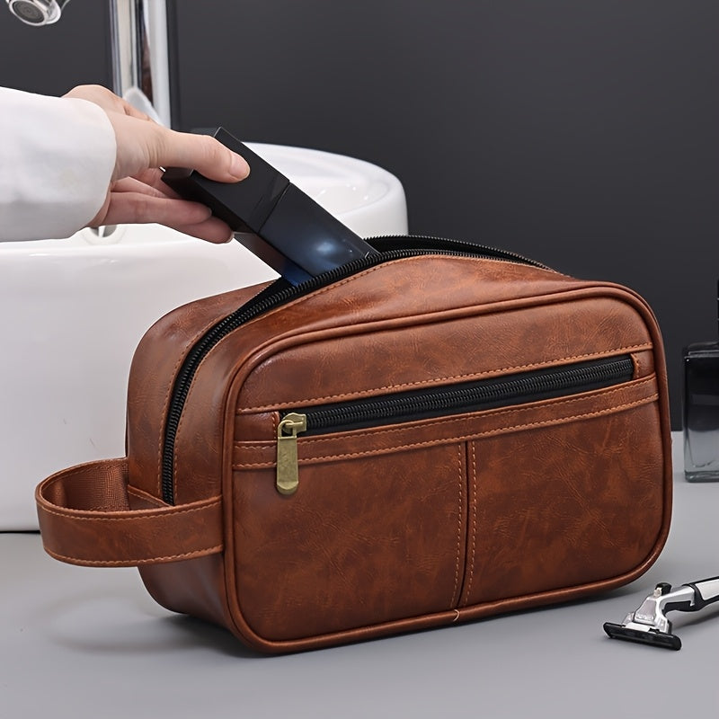 Brown leather toiletry bag with a hand reaching in to place a phone inside, on a gray surface.