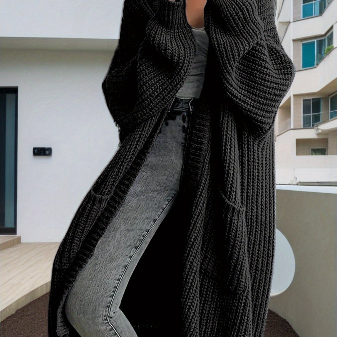Person wearing a long black knitted cardigan in an urban setting