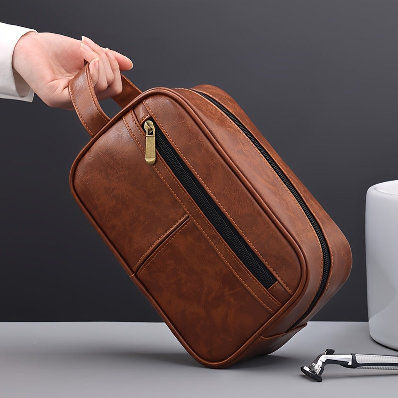 Brown leather toiletry bag with gold zipper held by a hand on a gray background