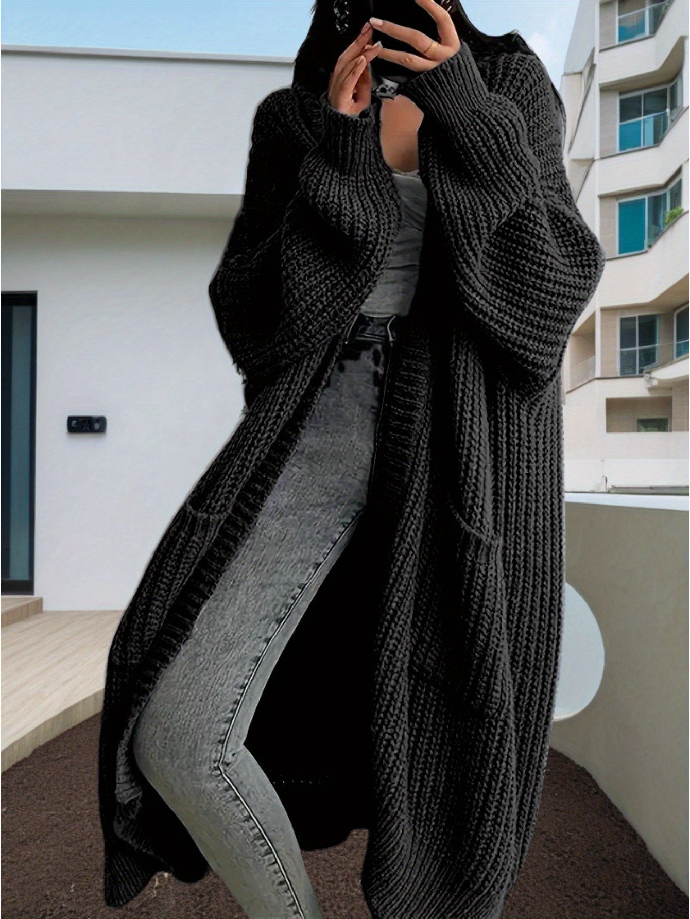Person wearing a long dark gray knitted cardigan in an urban setting