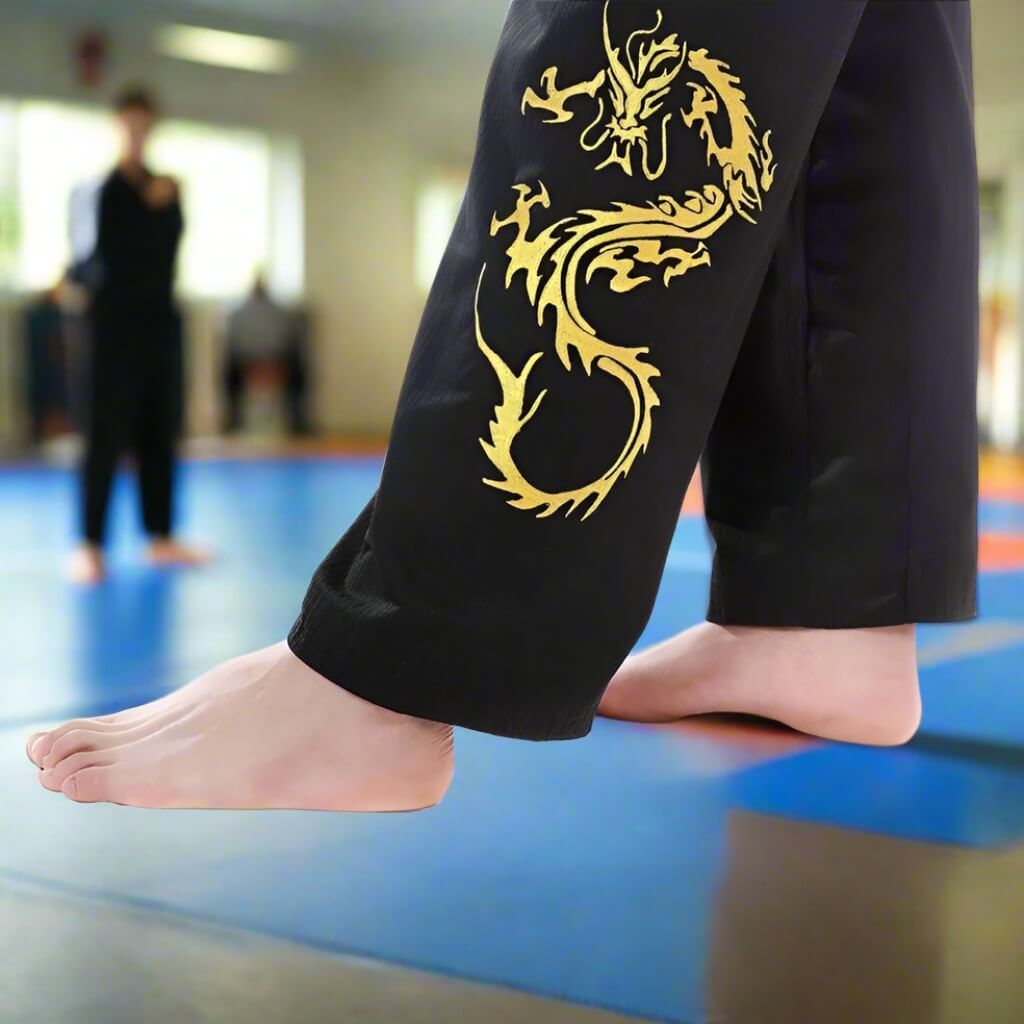Person wearing black pants with a gold dragon design in a martial arts setting.