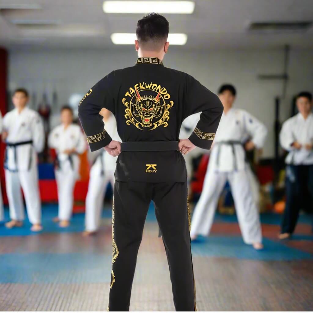 Person wearing a black Taekwondo uniform with gold designs in a martial arts classroom.