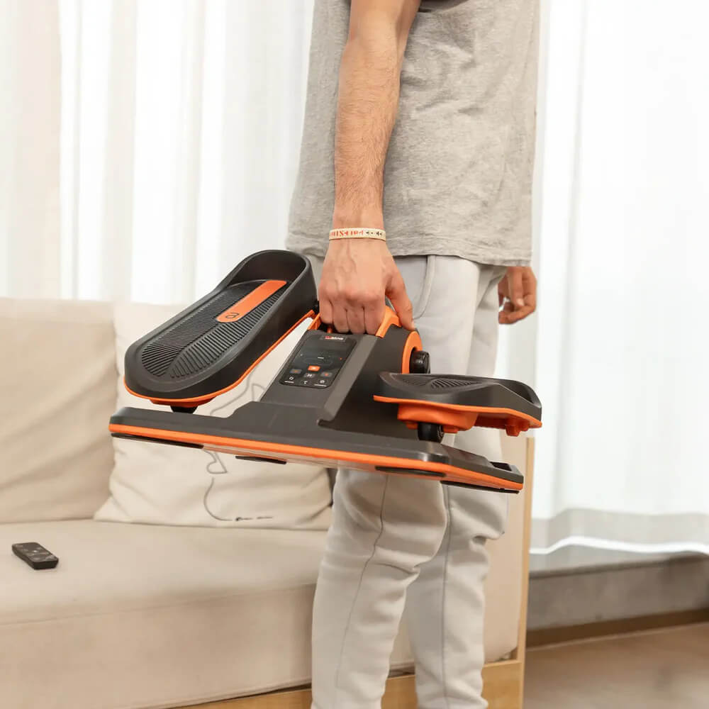 A man carrying an Under Desk Electric Elliptical Machine sold by 100 Spartans