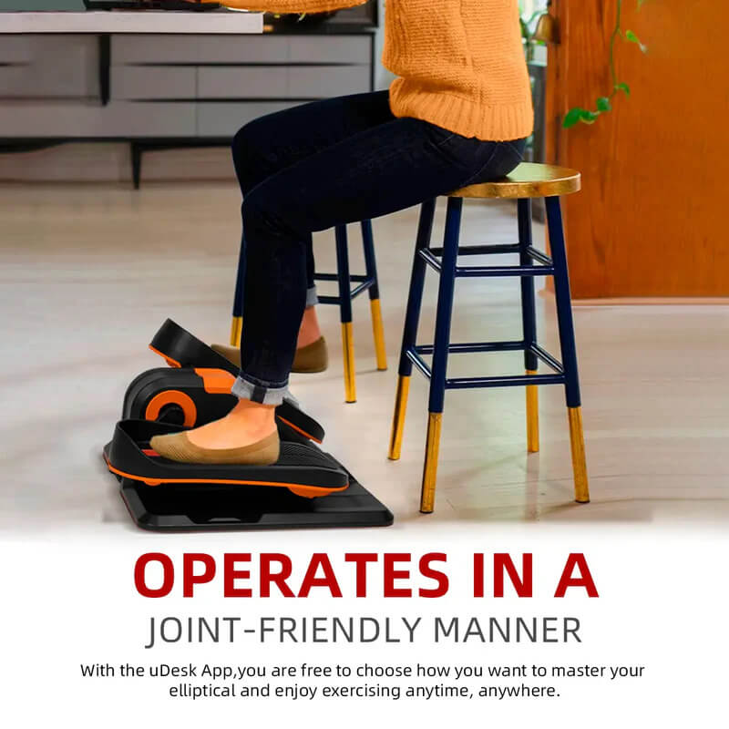 A person sitting on bar stool while exercising their legs on an under desk electric elliptical machine sold by 100 Spartans