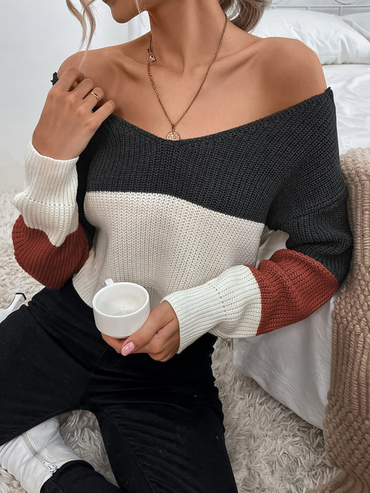 Person wearing a color-blocked off the shoulder sweater holding a mug indoors.