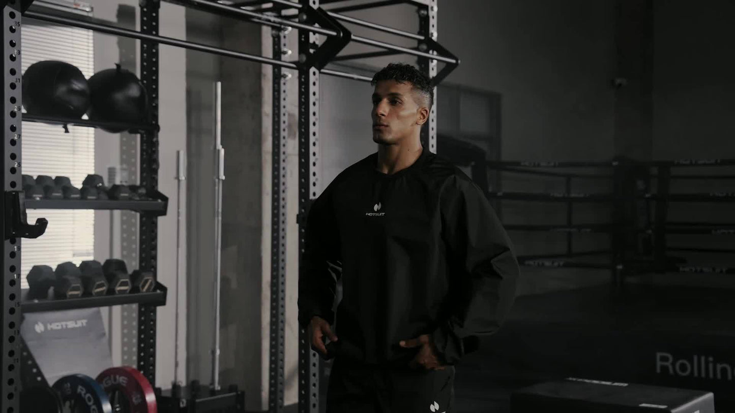 A man standing in a gym wearing a sauna sweat suit top, with weightlifting equipment in the background