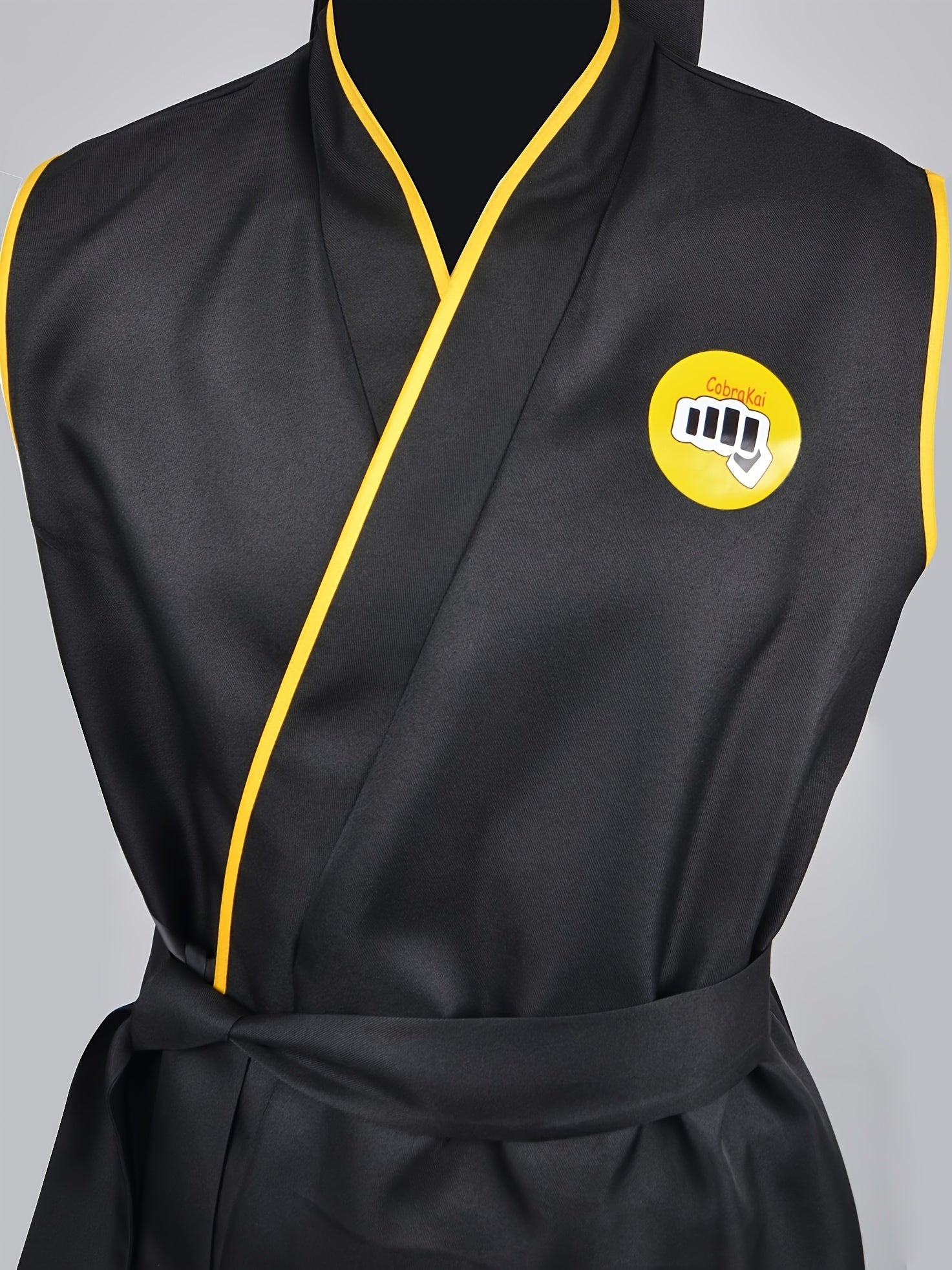 Black taekwondo uniform with yellow trim and a logo on a gray background