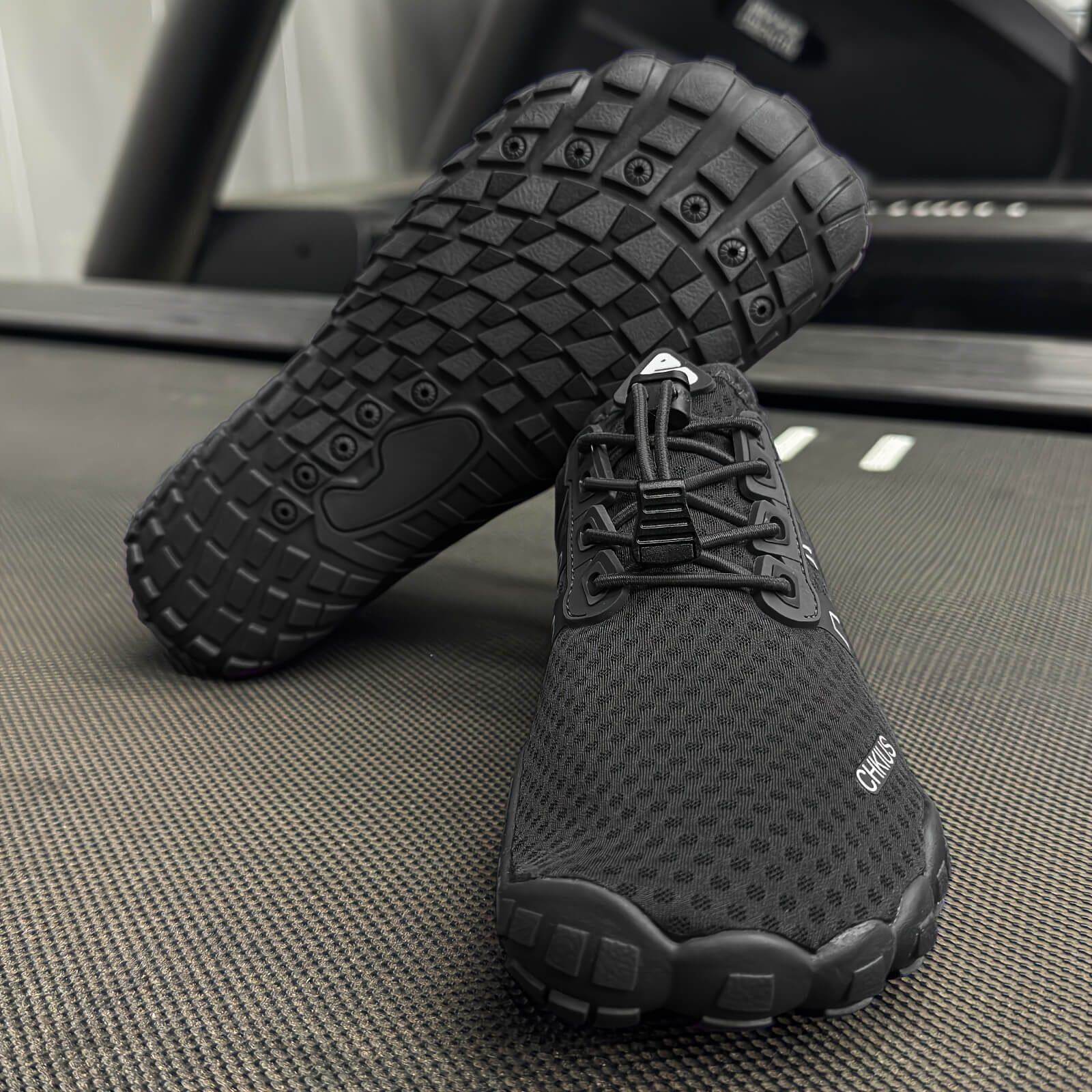 Black deadlift shoes with textured soles on a gray surface