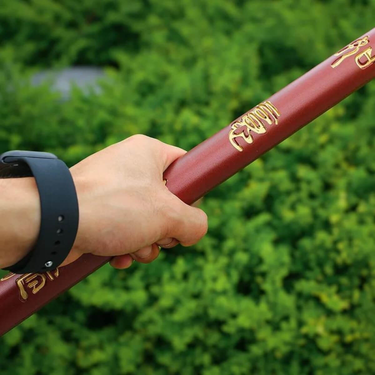 Hand holding a red Sun Wukong Stick  with gold text against a green blurred background