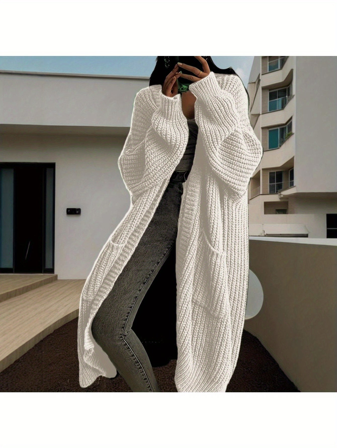 Person wearing a long white knit cardigan in an urban setting