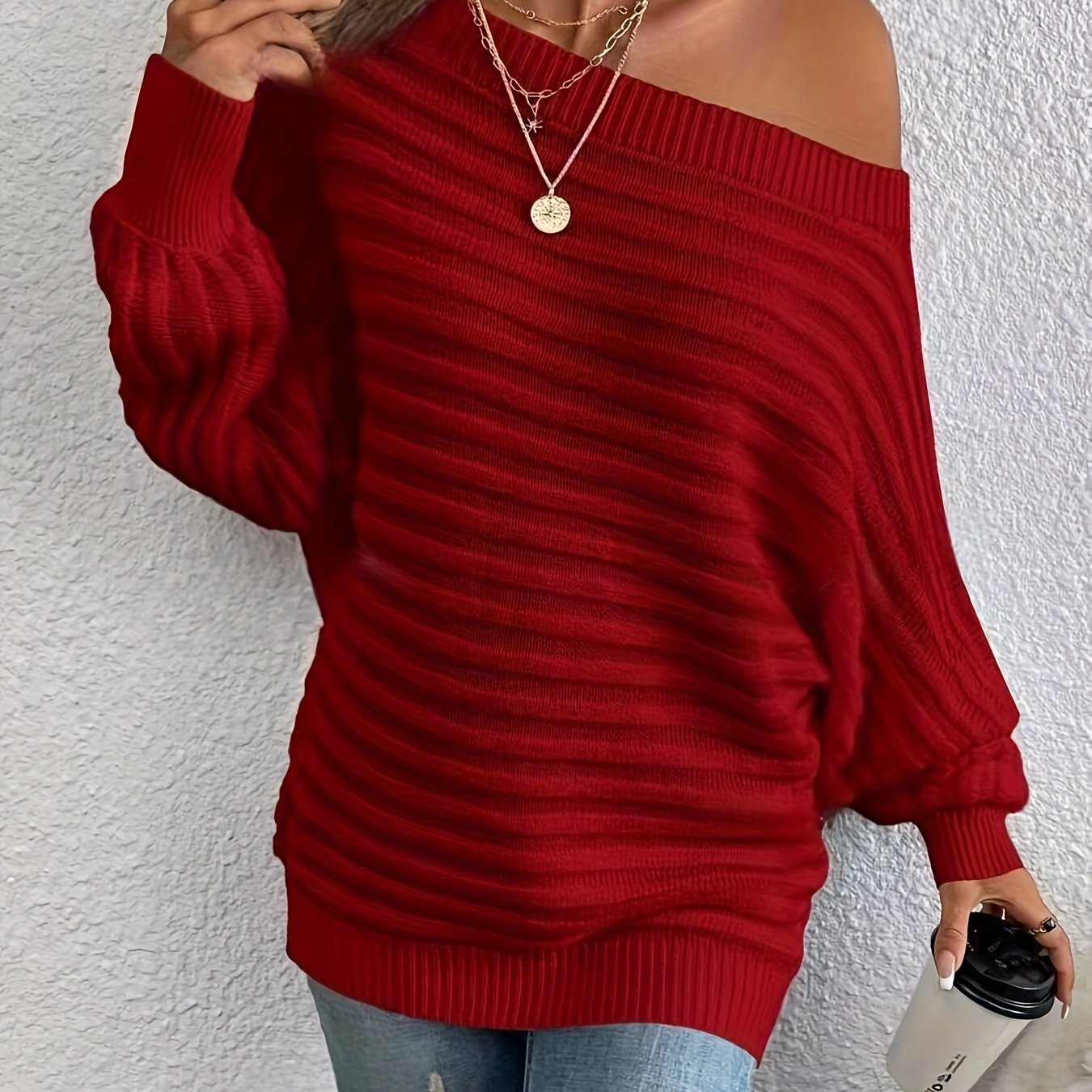 Red off shoulder sweater worn by a person against a white wall