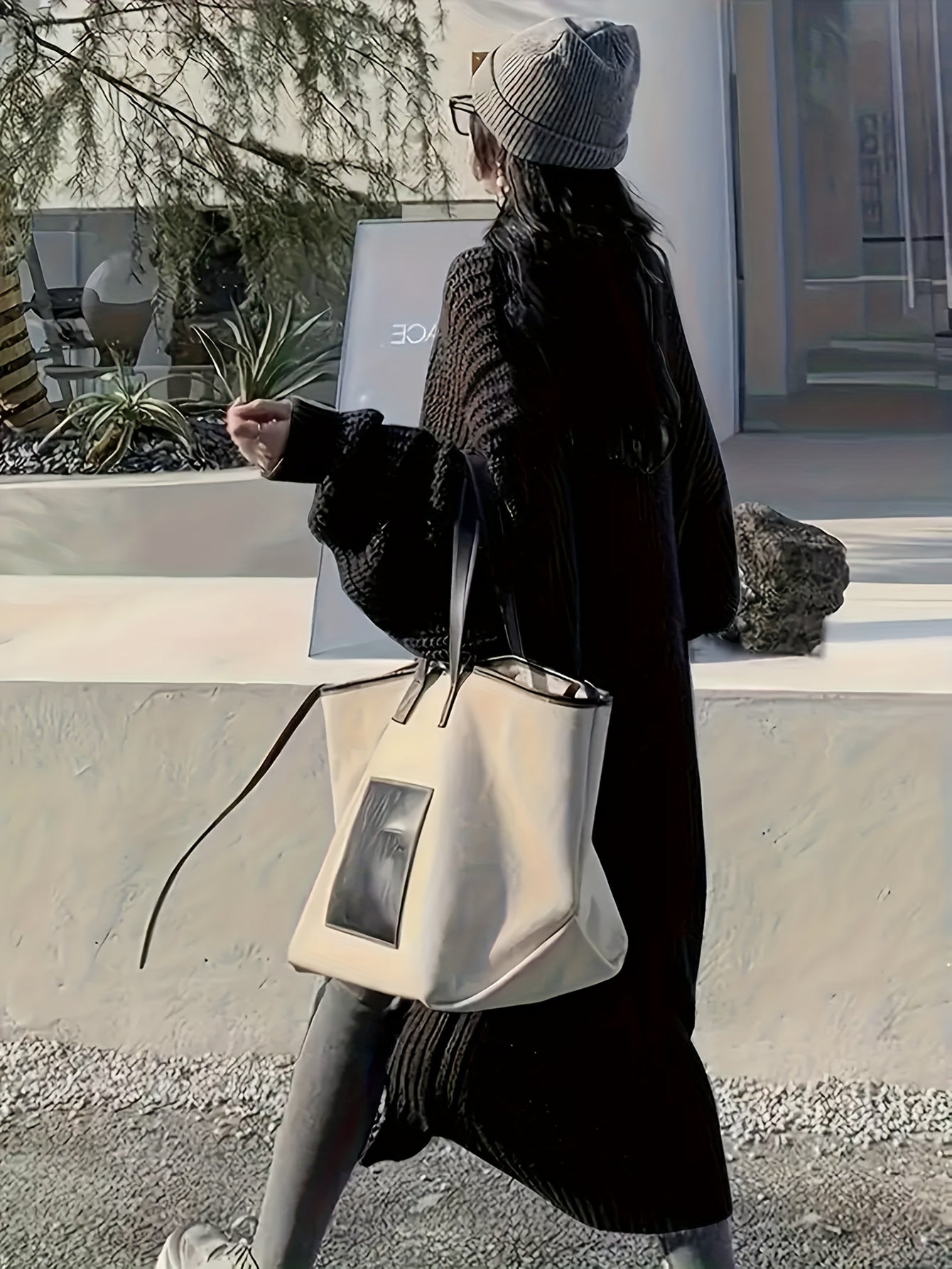 Person holding a white handbag outdoors with a building and plants in the background