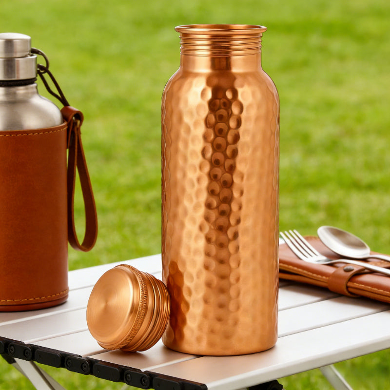 Copper water bottle with textured surface on a table outdoors