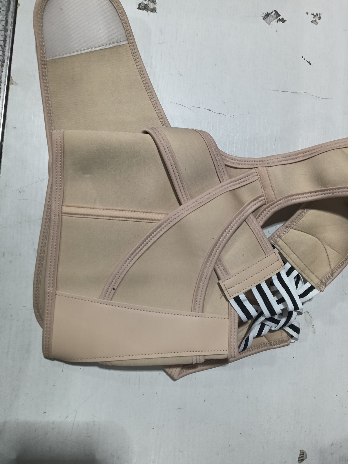 A beige posture corrector brace with adjustable straps, laid flat on a light gray surface.