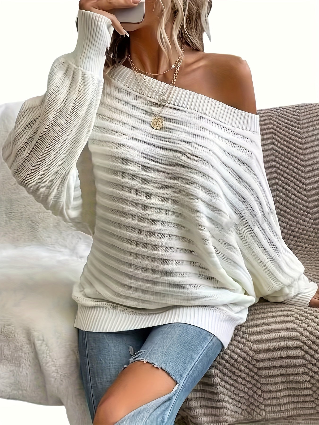 Person wearing a white off shoulder sweater sitting on a textured surface.