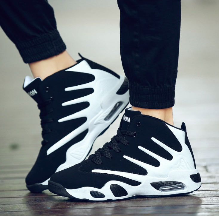 Black and white high-top sneakers worn with black pants on a wooden floor.
