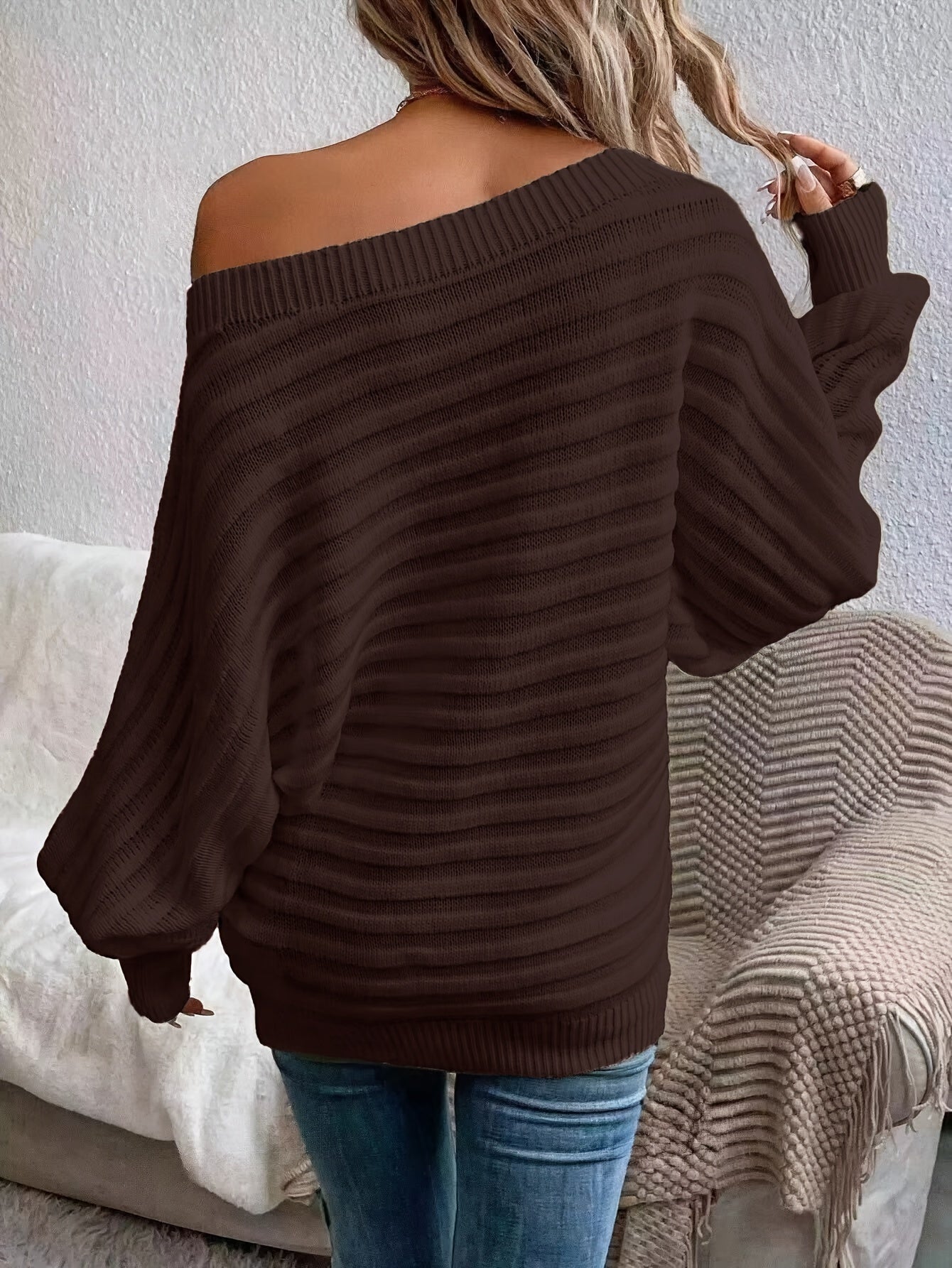 Person wearing a brown off shoulder sweater sitting on a couch.