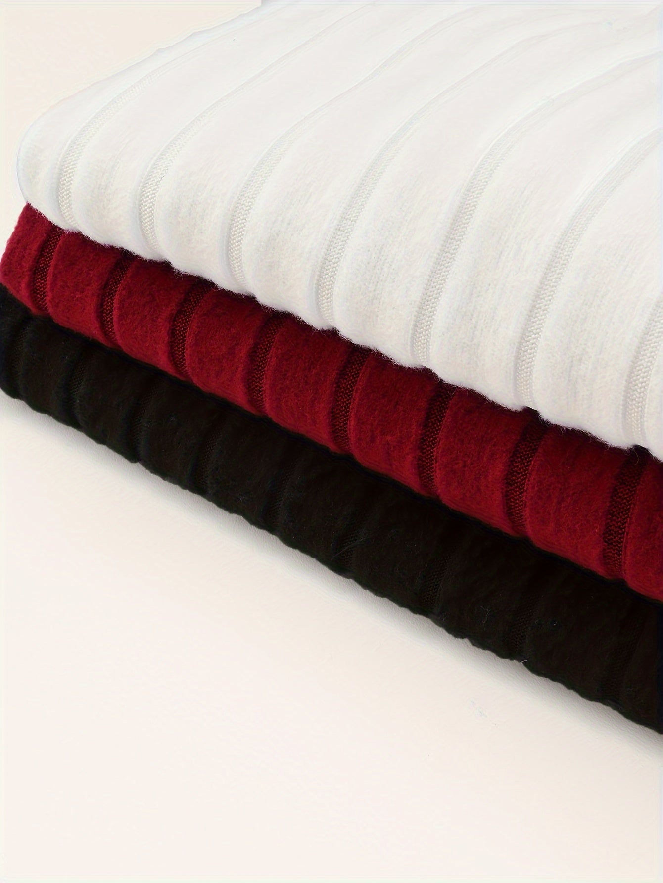 Stack of white, red, and black ribbed knit fabrics on a light beige background