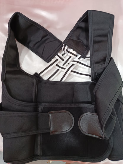 A black posture corrector brace with adjustable straps and hook-and-loop closures, laid flat on a light pink satin fabric background.