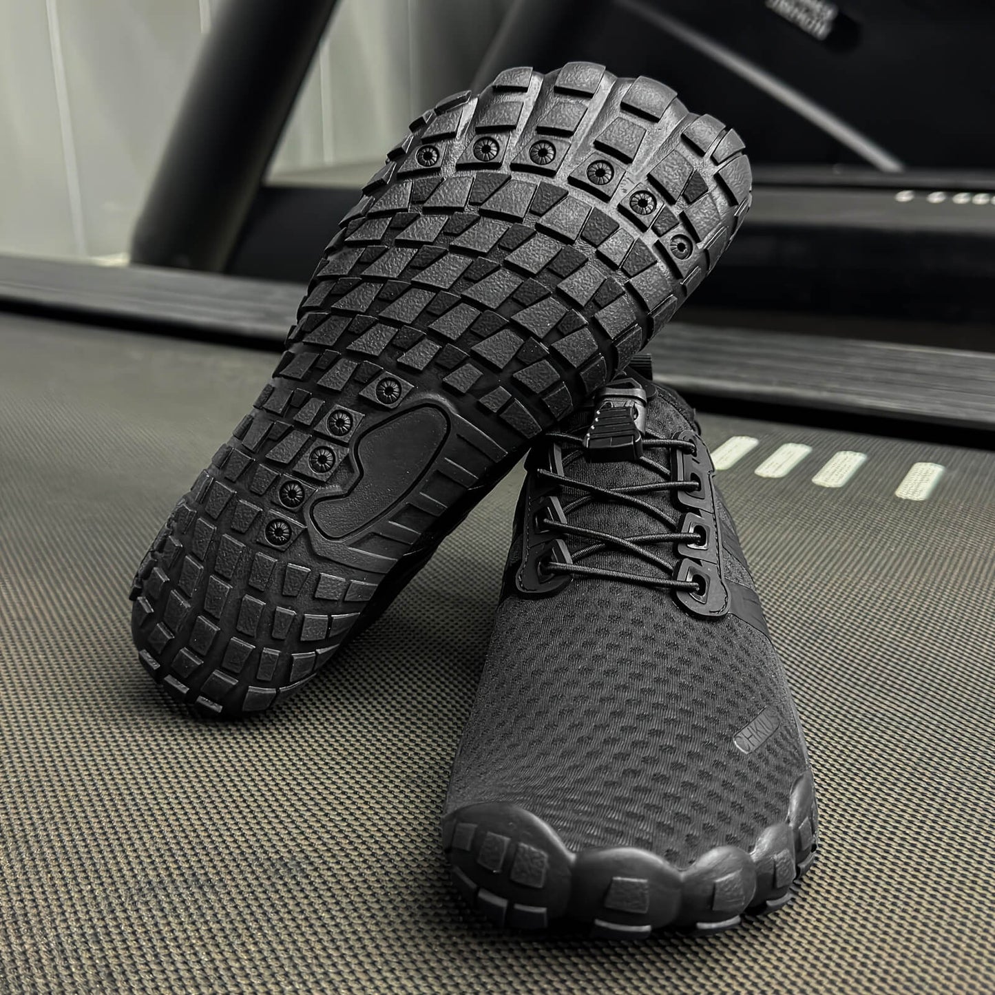 Black deadlift shoes with textured soles on a treadmill.