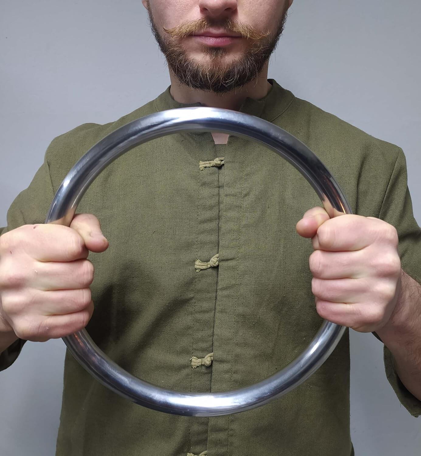 A man training with a wing chun ring in front of his face against a plain background