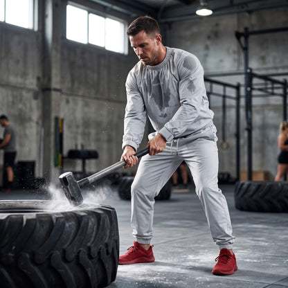 A white man doing sledgehammer trainning while wearing a light grey sauna suit.