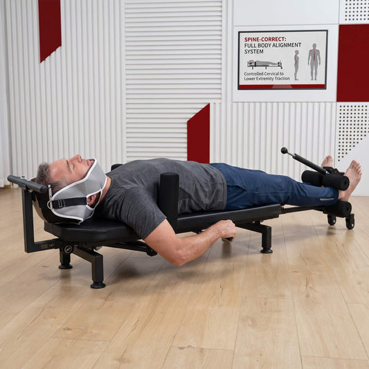 Person using a Full Body Stretching Machine with Cervical Traction & Spinal Decompression on a wooden floor with a white wall in the background.