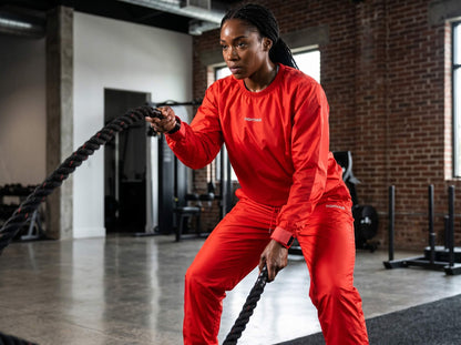 Person in red sauna suit using battle ropes in a gym setting