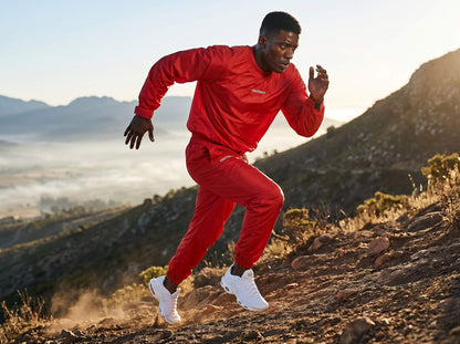 Man running on a mountain trail wearing a red sauna suit with a visible brand logo.