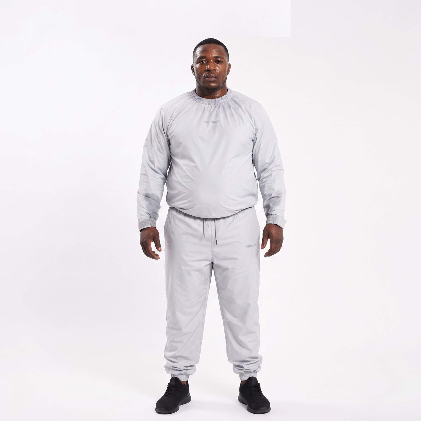 An overweight black man wearing a light grey sauna suit