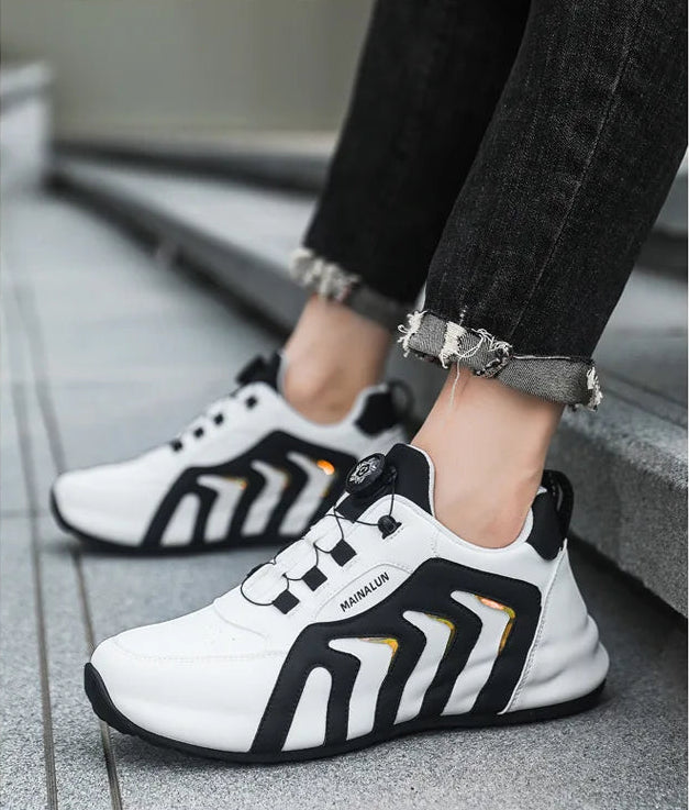 White and black athletic shoes worn with black pants on a gray floor.