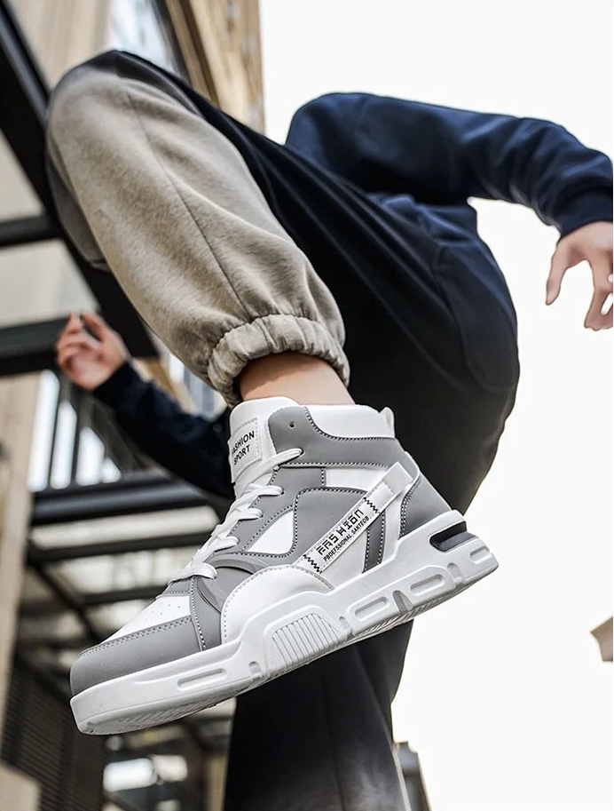 Gray and white high-top sneakers worn by a person with a blurred background