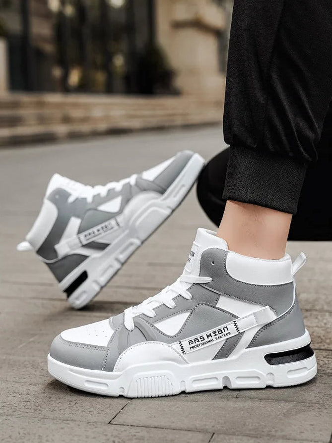 Gray and white high-top sneakers worn by a person on a sidewalk.