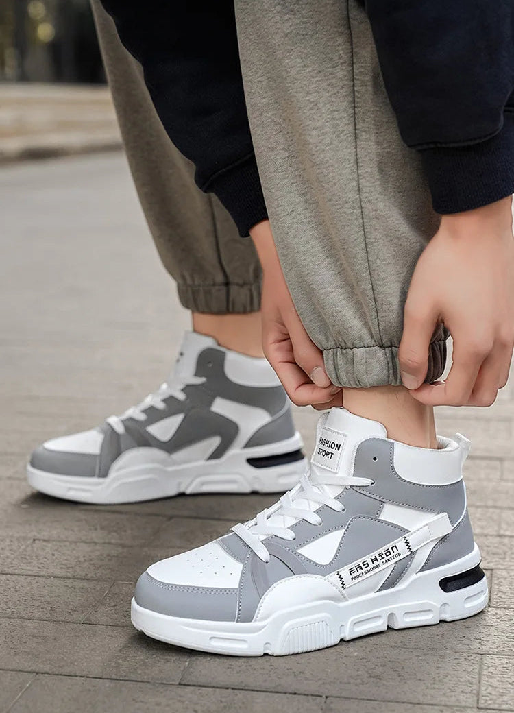 Gray and white sneakers worn by a person on a wooden floor.