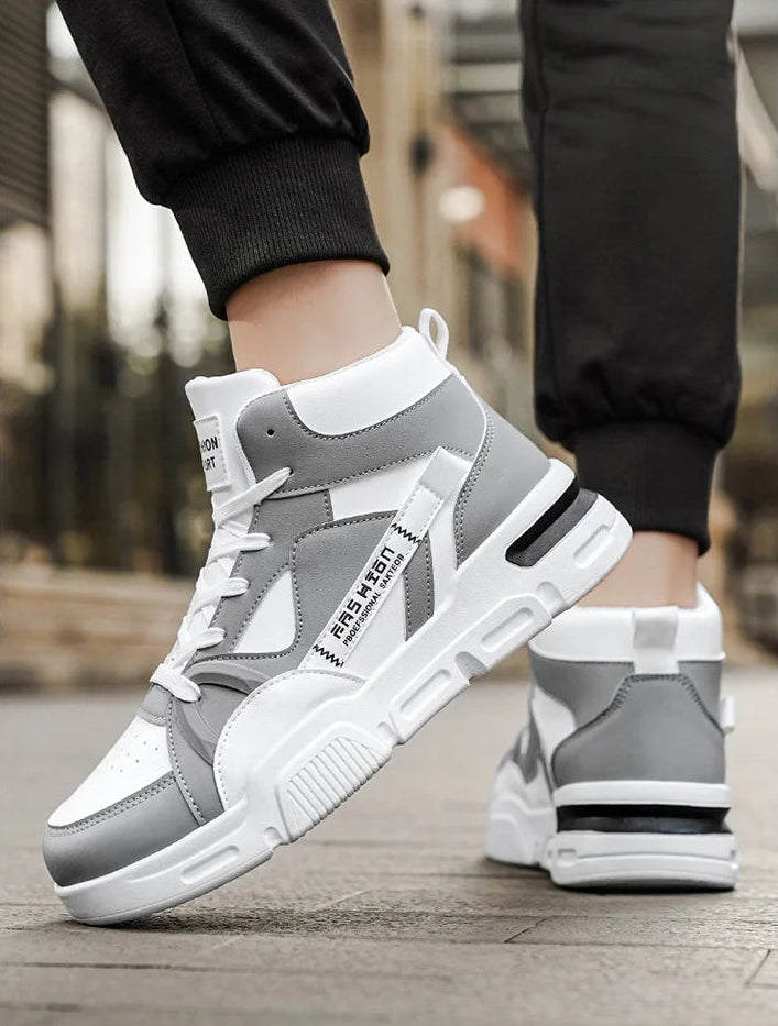 Gray and white sneakers worn by a person on a wooden floor.