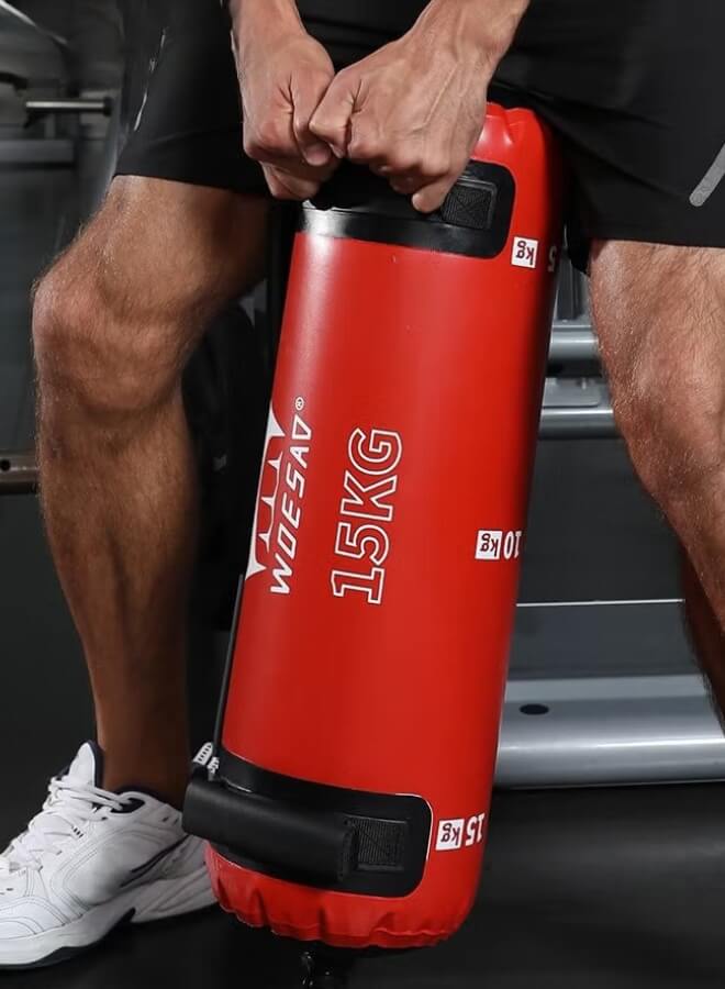 Person using a red water weight bag​ labeled '15KG' in a gym setting