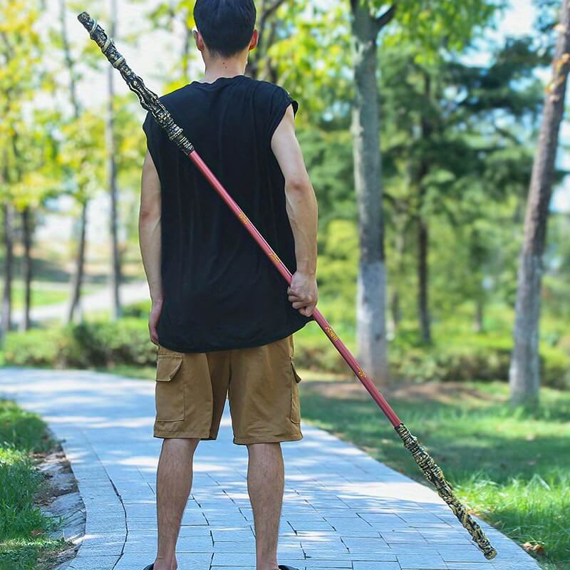 Person holding a large Sun Wukong Stick on a path in a park
