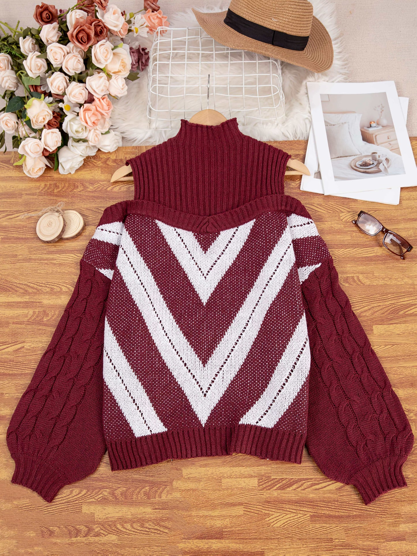 Maroon off the shoulder sweater with white geometric pattern on a wooden surface with flowers and a hat in the background