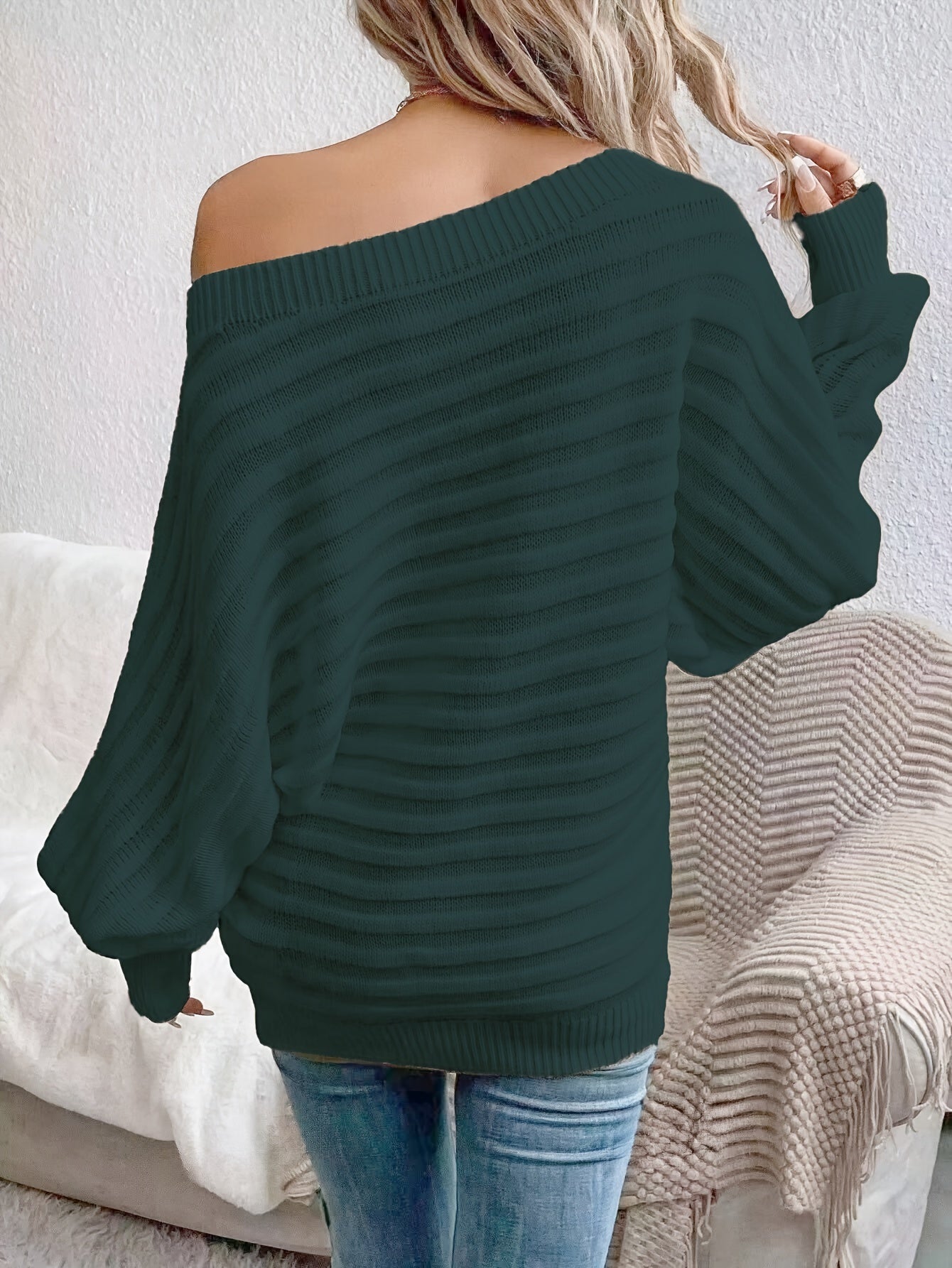 Green off shoulder sweater worn by a person, sitting on a couch with a neutral background