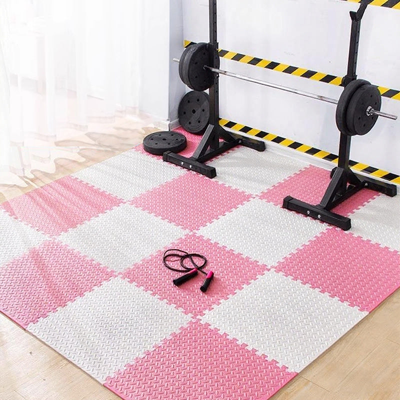 Pink and white checkered foam puzzle mat with weightlifting equipment on a wooden floor.