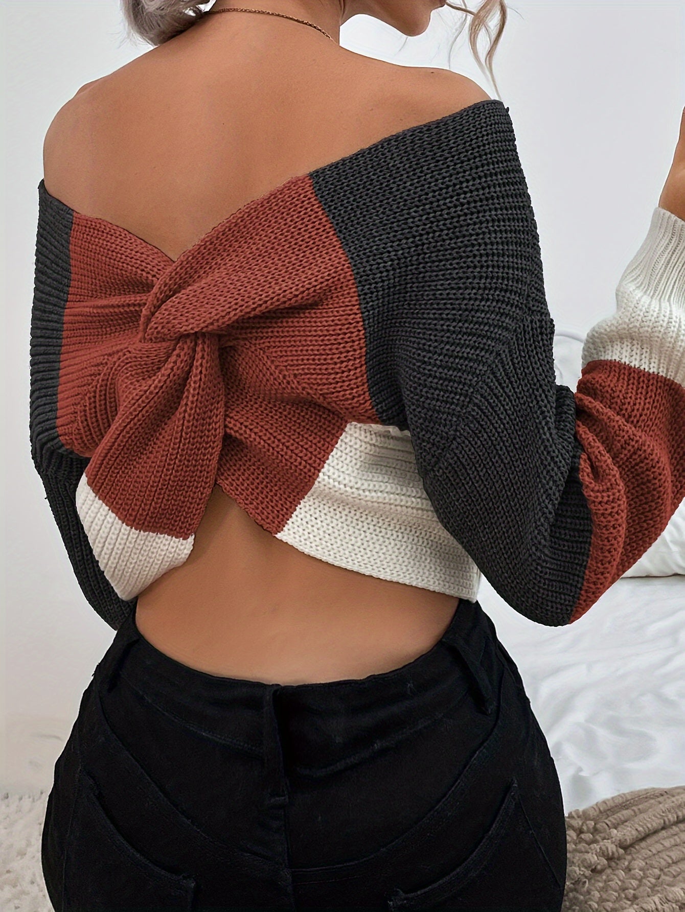 Woman wearing a colorful off the shoulder sweater with a knot design on a white background