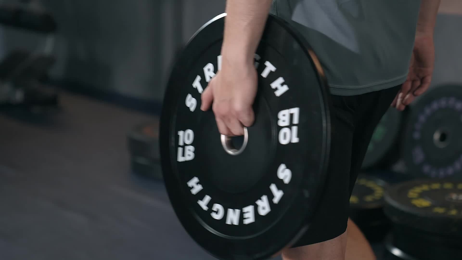 Person holding a black weight plate with 'Strength' branding in a gym setting