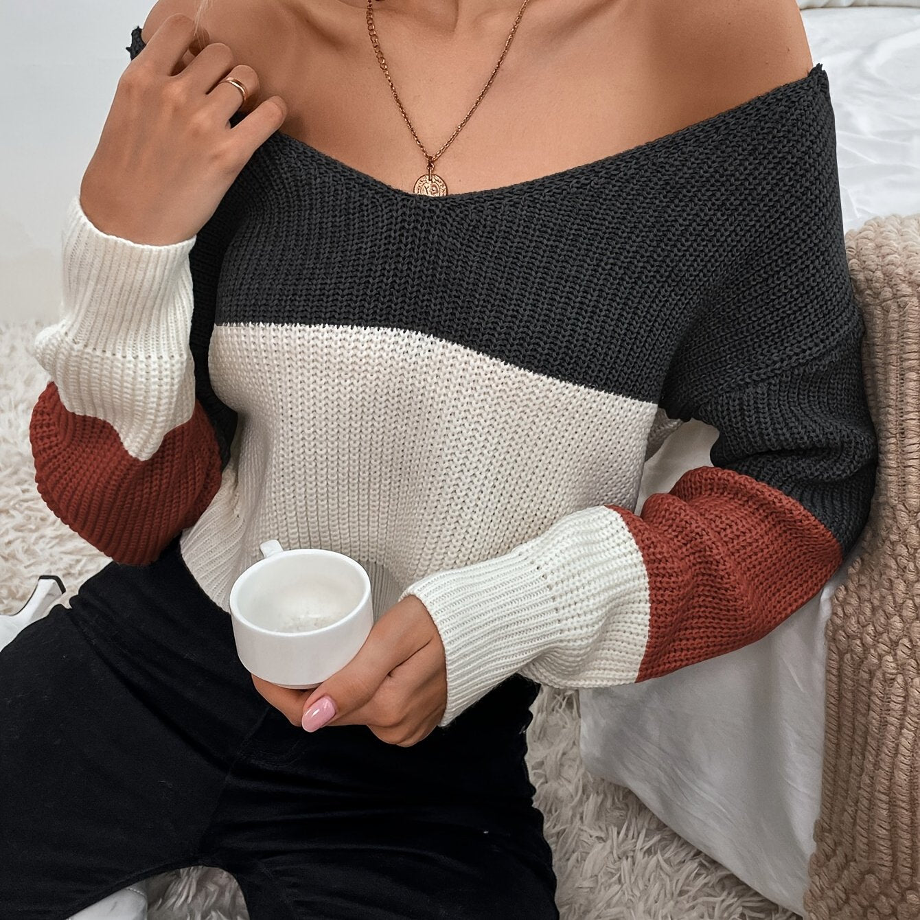 Person wearing a color-blocked off the shoulder sweater holding a white mug.