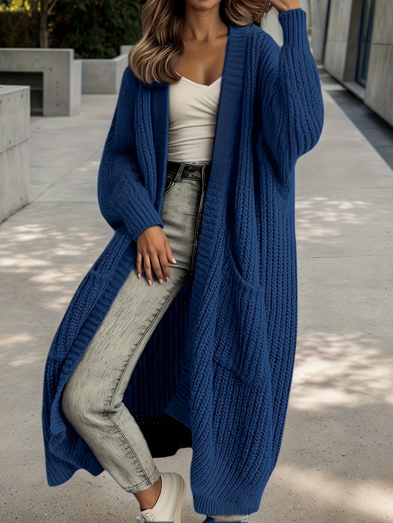 Person wearing a long blue cardigan over a white top and light jeans outdoors.